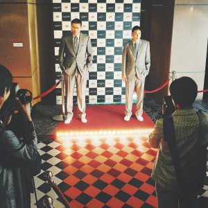 Yao Ming and Liu Xiang, dressed in matching suits, pose for photographers at an awards ceremony. Checkerboard floor with glowing red carpet and sponsor logos