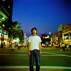 Jonghyun from the South Korean band SHINee, dressed in a casual outfit of a white t-shirt and jeans. Stands in a crowded urban street scene, night time