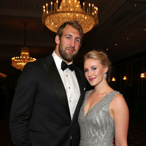 Chris Robshaw and Camilla Kerslake attending a gala. He in a black tuxedo, she in a silver sequined dress. Dimly lit room with chandeliers