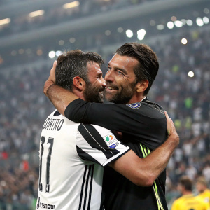 Gianluigi Buffon and Andrea Barzagli, Juventus FC teammates, sharing a hug after a match. A packed stadium in the background.