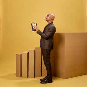 Jeff Bezos, standing in front of a minimalist white backdrop, dressed in a sleek black suit. He holds a tablet showcasing Amazon's latest customer-centric innovation.