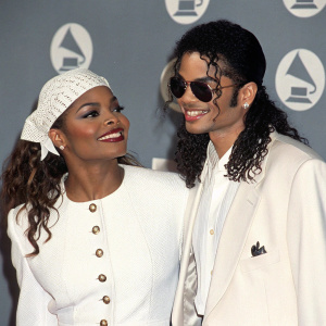 Janet Jackson and Michael Jackson at Grammy Awards, 1993. Janet in white outfit with head wrap, Michael in white shirt. Both smiling. Gray backdrop with faint Grammy logos