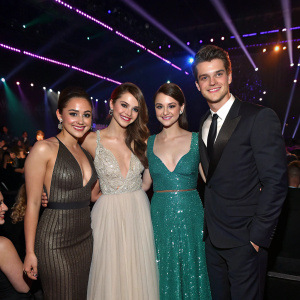 Francia Raisa, Greg Finley, India Eisley, Shailene Woodley, and Daren Kagasoff, all posing together at a glitzy awards show. The stage is dimly lit with colorful spotlights casting dynamic patterns on the backdrop.