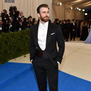 Chris Evans at the Metropolitan Museum of Art Gala. Dressed in a black tuxedo and white shirt. Blue carpet backdrop.