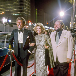 Dean Martin and Angie Dickinson standing together, Dom DeLuise on the right. They are at a Hollywood event, smiling and posing for the cameras.