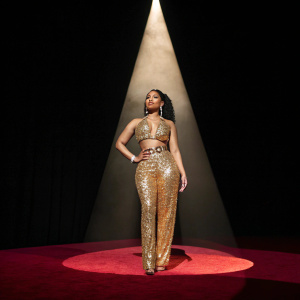 Nicki Minaj at Billboard Music Awards, wearing a gold sequined outfit. Black background, spotlight shining on her.