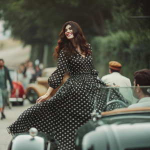 Italian actress Monica Bellucci, smiling gracefully, wears a black polka-dot dress. Poses in front of a bustling street scene during a fashion event.