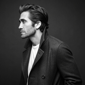 Jake Gyllenhaal, in a detailed monochrome photo. High cheekbones, chiseled jawline, and styled hair. Dark, uncluttered background.