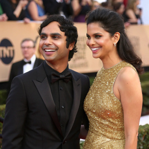 Kunal Nayyar and Neha Kapur at award show. He in a black tuxedo, she in a gold sequined gown. They're smiling for the paparazzi.