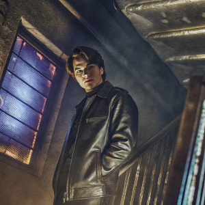 KJ Apa, young actor, wearing a black leather jacket. Dark and moody indoor setting with neon lights