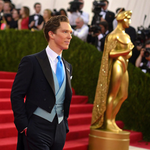 Benedict Cumberbatch at the Met Gala. Wearing a dark suit, vibrant blue tie, standing beside a golden statue.