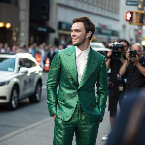 Nicholas Hoult, in a dazzling green suit and white shirt, poses for a paparazzi. Crowded street background