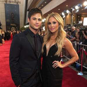 Cody Longo and Cassie Scerbo at a glitzy awards ceremony. Cody in a dark suit, Cassie in a black dress. Lavish red carpet surrounded by flashing cameras and enthusiastic fans.