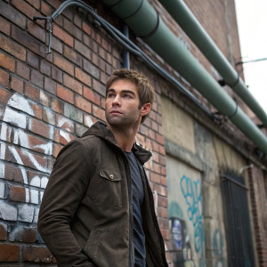 Chace Crawford, an actor, standing in front of a graffiti-covered brick wall with exposed pipes and ductwork. Serious expression, modern urban setting