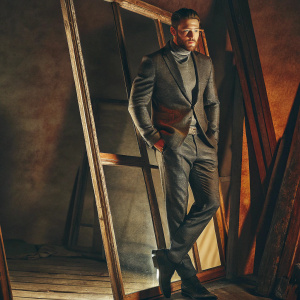 Julian Edelman, quarterback of New England Patriots, in a formal suit. Poses for a photo shoot inside a dimly lit studio.