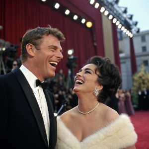 Burt Lancaster and Elizabeth Taylor laughing joyfully at the Oscars ceremony. Rich red carpet backdrop.