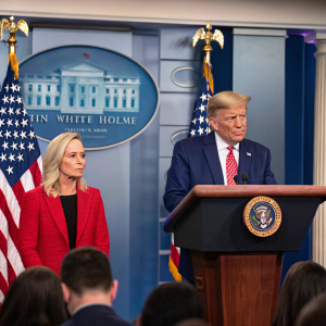 Donald Trump and Kirstjen Nielsen at a press conference. White House backdrop with American flag.