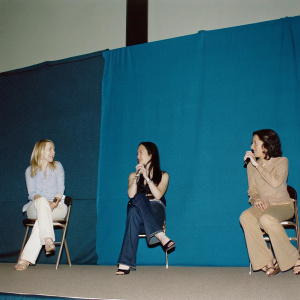 Kate Hudson, Lucy Liu, and Donna Freydakin discussing Kung Fu Panda at a Comic-Con panel. Casual outfits, diverse backgrounds, candid moment