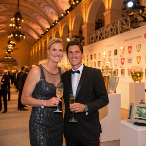Maria Hoefl-Riesch and Marcus Hoefl celebrating at the prestigious sports gala. The venue is decorated with sports memorabilia and awards.