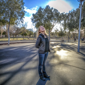Bonnie Somerville, blonde actress, in casual attire, standing in a sunlit park. Focused shot, natural surroundings.