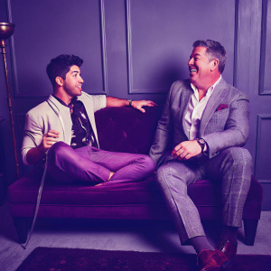 Nick Jonas and Elvis Duran sharing a casual chat. Studio with dark grey backdrop and logos