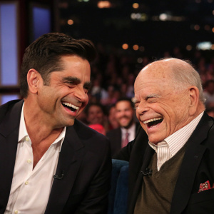 John Stamos and Don Rickles laughing on Jimmy Kimmel's talk show set. Studio audience in the background.