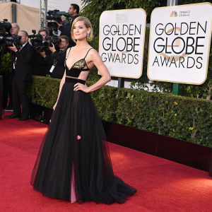 Rosamund Pike at the Golden Globe Awards, wearing a stunning black gown with pink details. She poses confidently on the red carpet surrounded by flashing cameras.