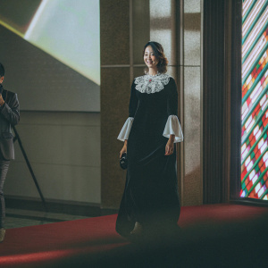 Yoona, wearing a black gown with white ruffled collar, graces the red carpet at a glamorous award show. Multicolored, abstract backdrop