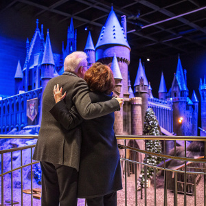 Jerry Weintraub and Carla Gugino, embracing at the Warner Bros. Studio tour London - The Making of Harry Potter. The Hogwarts castle model in the background.