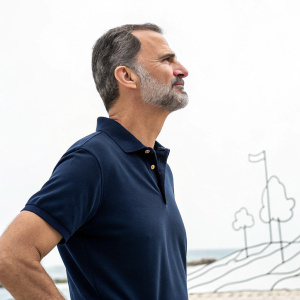 King Felipe VI of Spain in a navy blue polo shirt. Gazing off into the distance. Simplistic black background