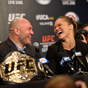 Dana White and Ronda Rousey, both laughing, at a UFC press conference. Ronda with short, straight hair, Dana wearing a suit.