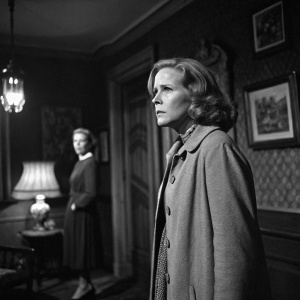 Vintage black and white still from 'The Night Visitor' (1971) featuring Liv Ullmann and her co-star. They are standing in a dimly lit room with vintage decor.