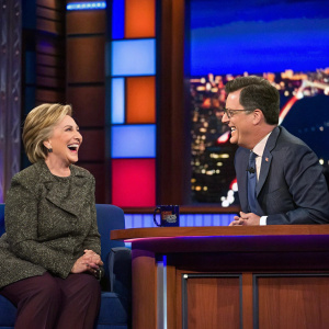Hillary Clinton and Stephen Colbert in a vibrant studio. Late night talk show atmosphere.