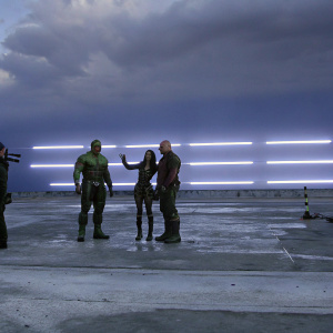 Chris Pratt, Zoe Saldana, Dave Bautista, and Vin Diesel standing on the set of Guardians of the Galaxy. Neon lights and graffiti in the background.