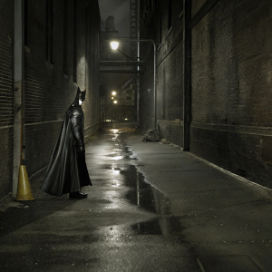 Batman standing alone in a rain-soaked Gotham alley. The dark, atmospheric setting with only faint streetlights casting shadows.