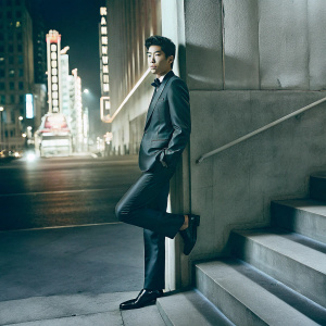 Chinese actor Li Yifeng on the set of a high-profile movie premiere. He is dressed in a sleek, dark suit, against a backdrop of neon lights and bustling city skyline.