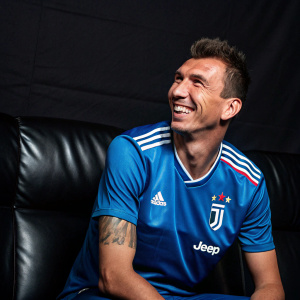 Mario Mandzukic, Croatian soccer star, grinning. Wears Juventus FC blue jersey. Against sleek, all-black backdrop.