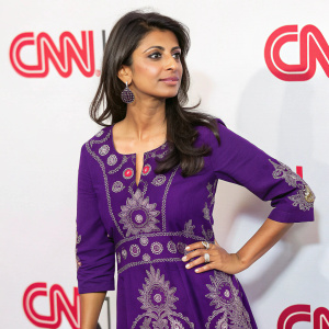 Konnie Huq, of South Asian descent, wearing a vibrant purple dress with intricate designs, interviewing for CNN. White backdrop with bold CNN logos. Direct gaze.