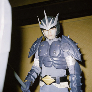 High detail figurine of Kamen Rider Agito, heroic pose. Gray armor with sharp points, dark background.