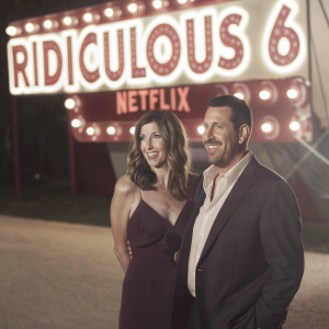 Adam Sandler and Jackie Sandler at an outdoor premiere for 'The Ridiculous 6' on Netflix. They are standing in front of a bright, illuminated backdrop.