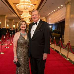 Ken Howard and Linda Fetter, a stylish couple, posing at a glamorous charity gala. The venue is adorned with chandeliers and red carpets.
