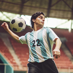 Paulo Dybala, Argentina jersey, number 22, dynamic pose with soccer ball. Indoor stadium, blurred seating areas, reddish hue, moment of action