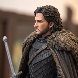 Jon Snow, detailed Game of Thrones collectible figurine. Dark hair, serious expression. Dark medieval outfit with fur-lined cape. Sword at his side. Close-up view