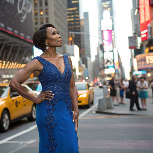 Angela Bassett, wearing an elegant blue dress with intricate beadwork, poses in front of a bustling New York City street.
