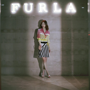 Lee Da-hee, South Korean actress, attending the Furla Fashion Show. Wearing vibrant multi-colored blouse paired with black and white striped skirt. Bright and colorful backdrop featuring Furla logo.