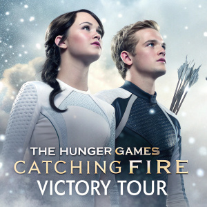 Poster for 'The Hunger Games: Catching Fire'. Katniss Everdeen and Peeta Mellark standing together. Soft, white particles background. Promotional text at bottom about victory tour.