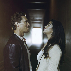 Close-up photo of Matthew McConaughey and Camila Alves. Matthew, a lean Caucasian male, and Camila, a woman of Hispanic ethnicity, both dressed in dark clothing. Dark, blurred background.
