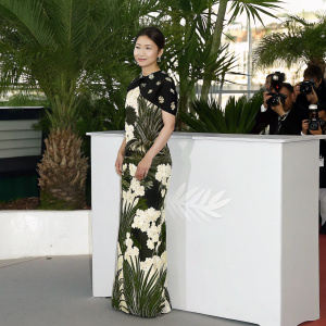 Shin Se-Kyung at Cannes Film Festival. Wearing elegant black and gold floral dress. Background is red carpet event.