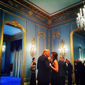 Melissa Gallo and Donald Trump at a high-profile political fundraiser. The venue is opulent with gold accents and chandeliers.