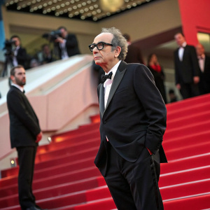 Cinematic genius Jean-Luc Godard, dressed in dark suit and glasses, at Cannes Film Festival.